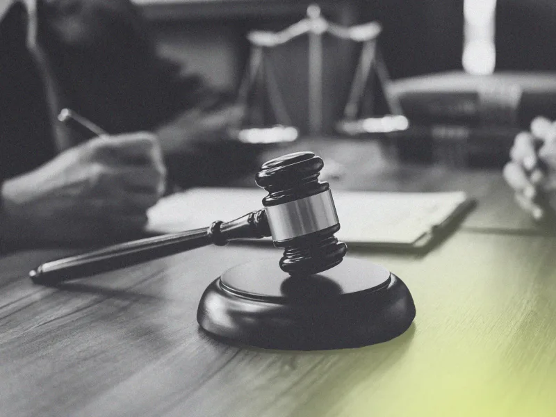Person writing on a notepad with a gavel and scale on the desk