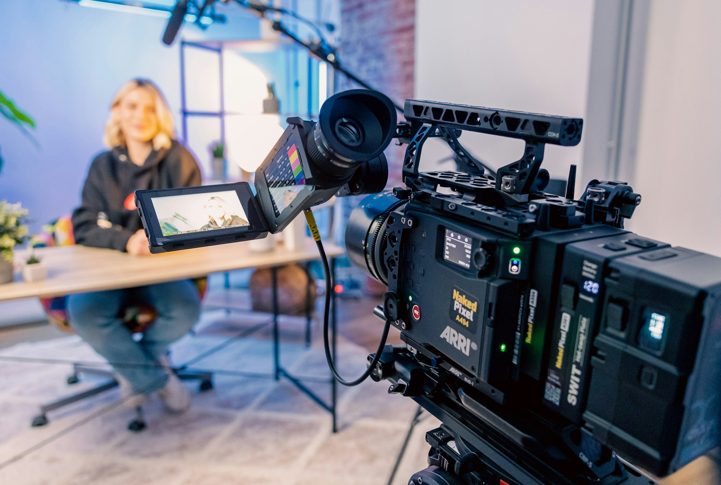 A cinema camera filming a content creator at her desk, with a monitor showing the live framing.